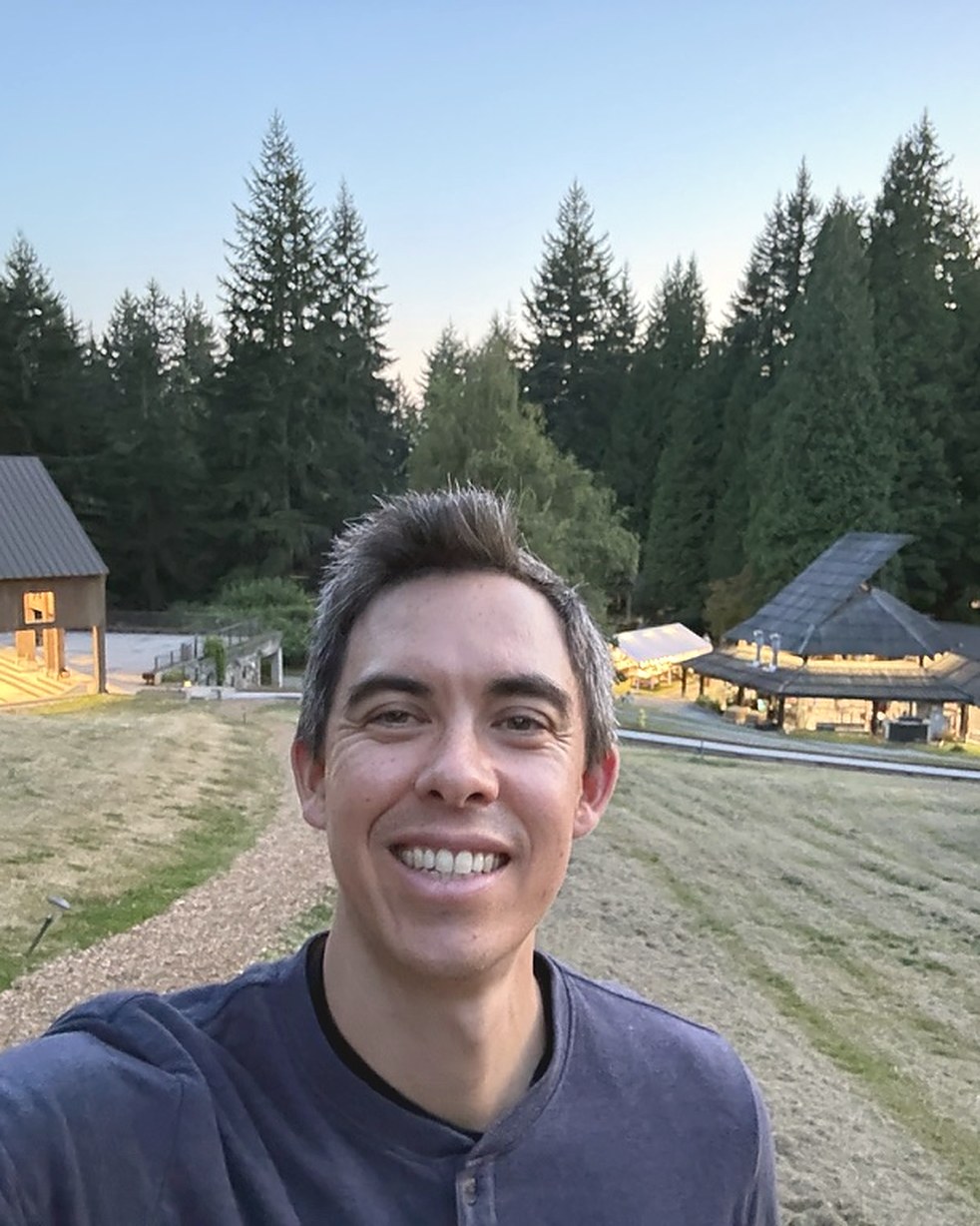 Naoki Sullivan at dusk on the Pilchuck Glass School campus, with the hot shop pavilion and fir forest behind him.